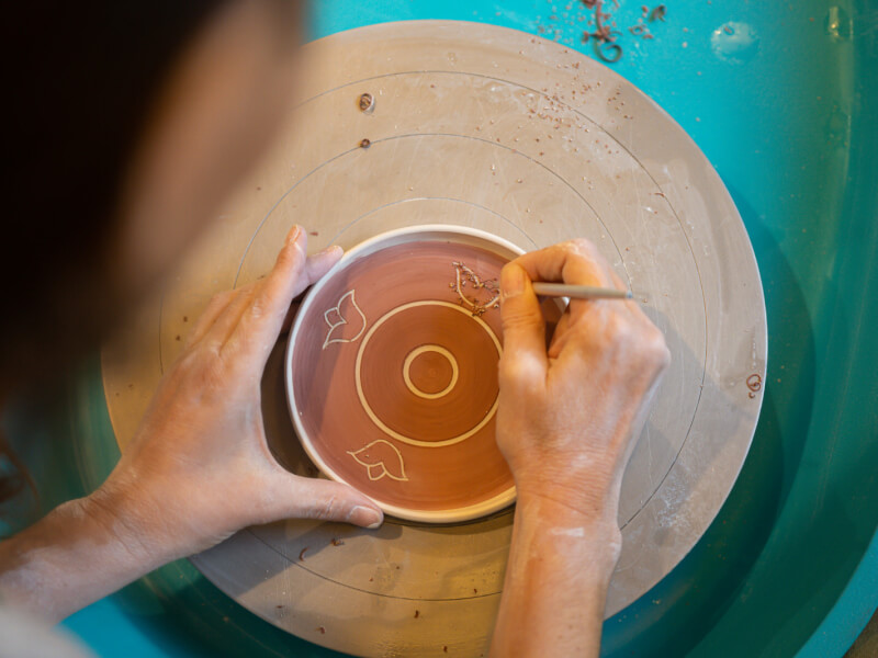 A close up of a person using the sgraffito technique to scratch a design onto a piece of pottery